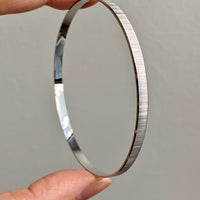 A vintage Italian 18k white gold solid bangle with scribed line pattern, held between fingers, showing the interior and exterior surfaces.