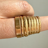 18k Gold rings with intricate designs on a finger against a neutral background