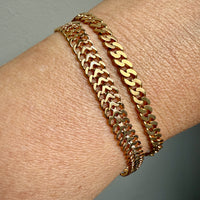Gold chain bracelet on a wrist with a neutral background