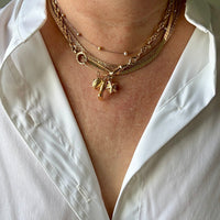 Gold necklace with charms on a person wearing a white shirt.