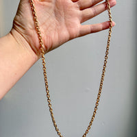 Gold chain held by a hand against a gray background