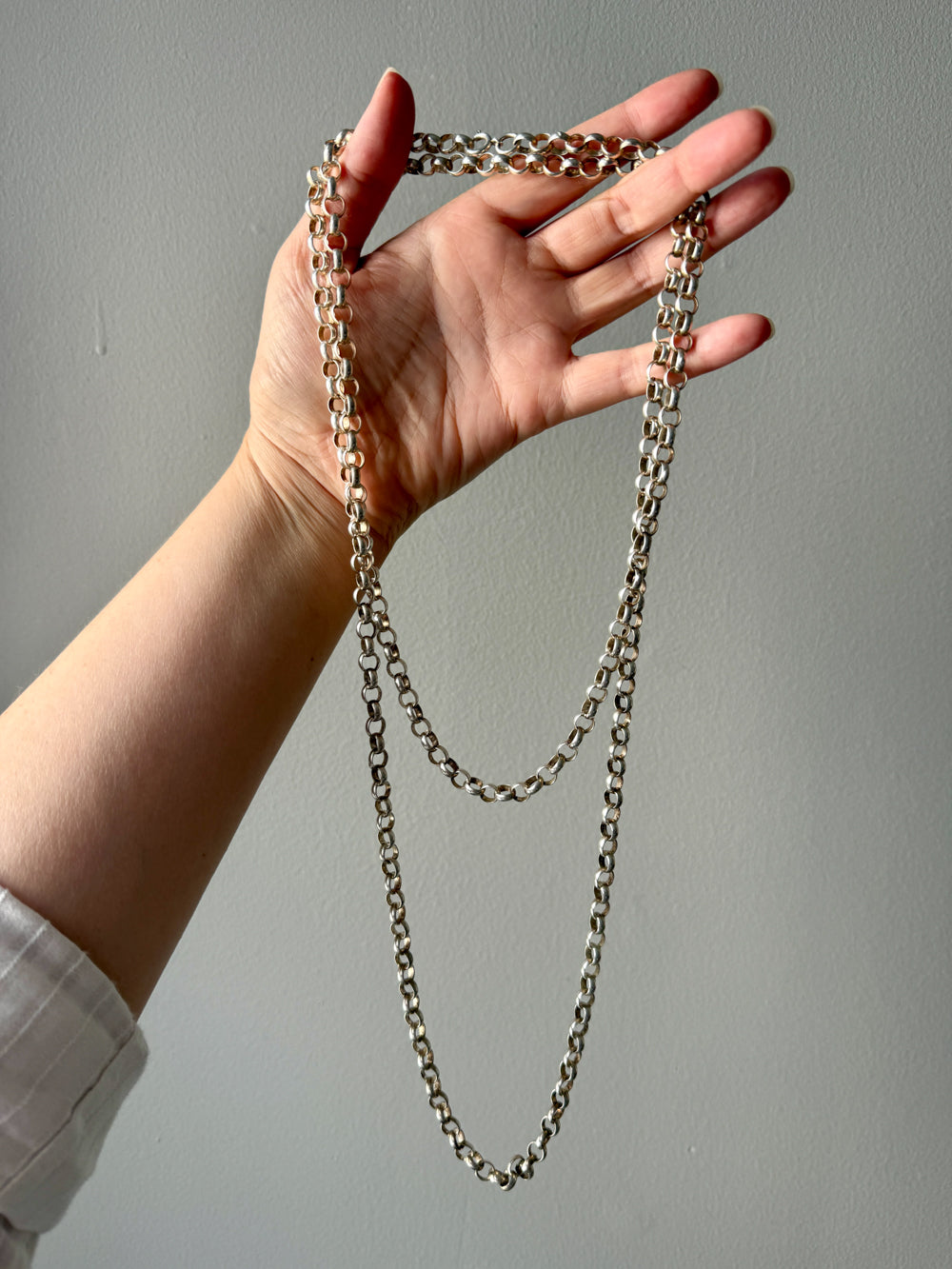 Hand holding a long chain necklace against a plain background