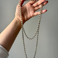Hand holding a long chain necklace against a plain background
