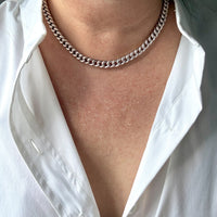 Person wearing a silver curb chain necklace with a white shirt