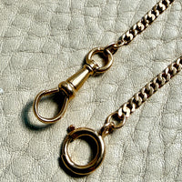 Gold watch chain with clasp on a textured light gray background