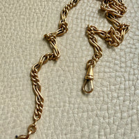 a french antique watch chain necklace in 18k gold displayed on a textured off-white surface.