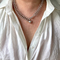 Person wearing a silver chain necklace with a white shirt.