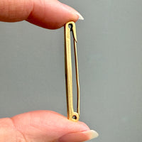 Gold safety pin held between fingers against a gray background