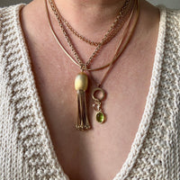 Necklace with tassel and green pendant worn by a person in a textured garment.