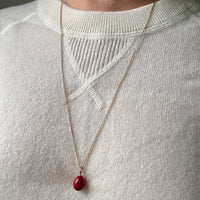 Necklace with a red pendant worn by a person on a plain background