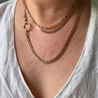 Close-up of a person wearing gold chain necklaces on a plain background PenelopePenelope.com