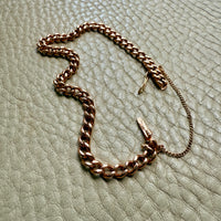 Rose gold chain bracelet on a textured light gray surface
