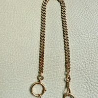 Gold chain with bolt clasps on a textured light gray background