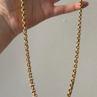 Gold chain held by a hand against a plain background penelopepenelope.com