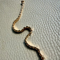 18k gold snake-shaped bracelet on a textured gray surface