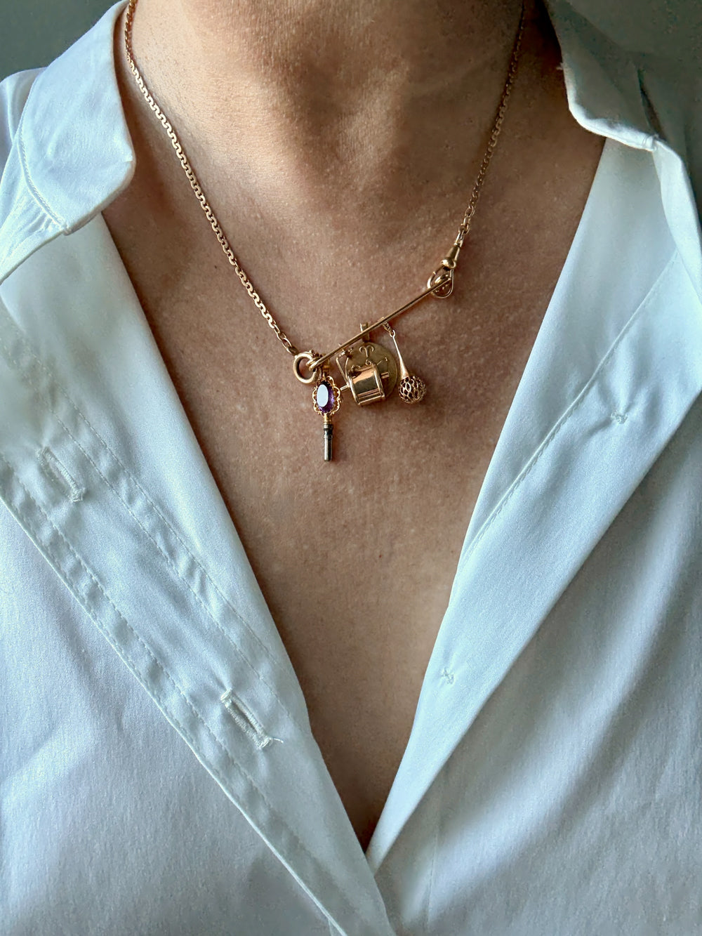 Gold necklace with charms pendant worn by a person in a white shirt