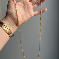 Gold chain held by a hand against a gray background