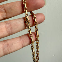 Gold biker link chain held in a hand against a plain background