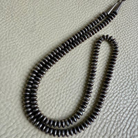 Silver beaded necklace on a textured beige surface