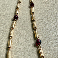 Gold necklace with red beads on a light gray textured background