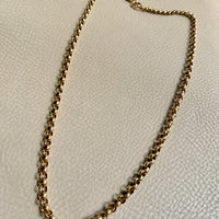 Gold chain necklace on a light beige textured surface