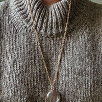 Necklace with a pendant worn on a person wearing a gray knit sweater.