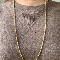 Gold chain necklace on a person wearing a brown sweater
