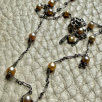 french antique platinum Necklace with pearl beads on a textured beige surface