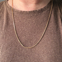 Gold chain necklace worn by a person on a plain background