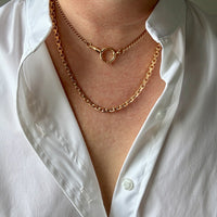 Person wearing a gold chain necklace with a white shirt