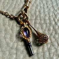 Necklace with key-shaped pendant and purple gemstone on textured surface