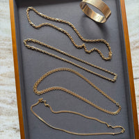 Gold jewelry including a bracelet and two necklaces displayed in a wooden box with a gray interior.