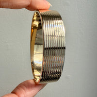 Gold bangle held by a hand against a gray background