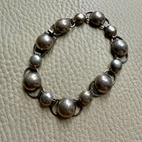 A silver bubble link bracelet laid out on a textured surface, showcasing its circular links and clasp.