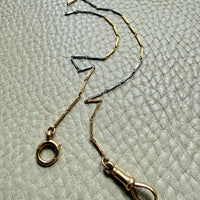 18k Gold and platinum watch chain with clip on a textured beige background
