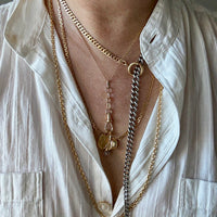 Close-up of a person wearing multiple gold necklaces with a white shirt.