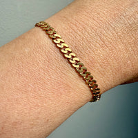 Gold chain bracelet on a wrist with a neutral background