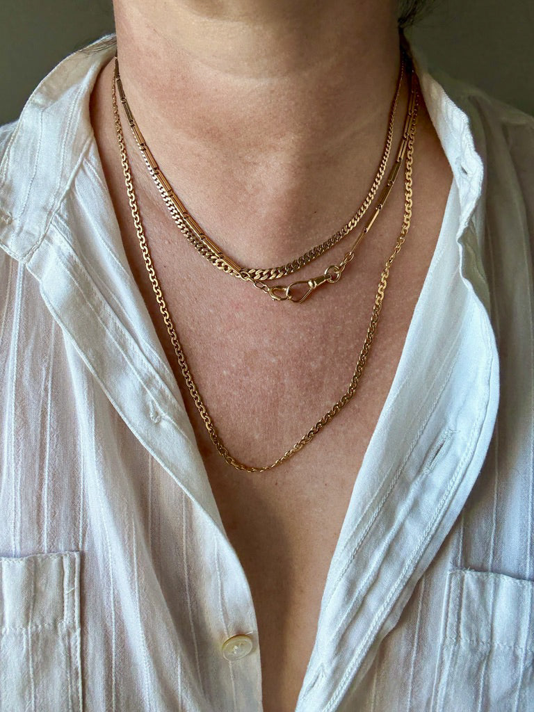 Close-up of a person wearing multiple gold necklaces with a white shirt.