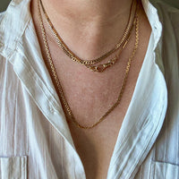 Close-up of a person wearing multiple gold necklaces with a white shirt.
