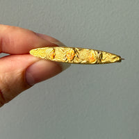 14k Gold enamel brooch with intricate design held by a hand against a plain background