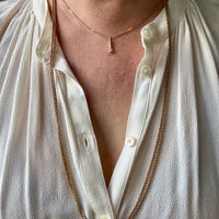 Person wearing a long gold necklace with a white shirt.