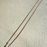18k gold watch chain necklace with dog clip on a textured light gray background