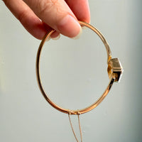 Gold bracelet with a clasp held by a hand against a light background