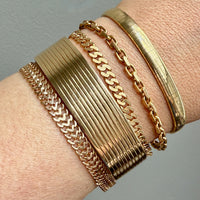 Gold bracelets on a wrist against a gray background