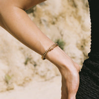 Close-up of a person's arm with a gold bracelet against a blurred natural background