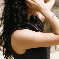 Woman with long dark hair covering her face, wearing a black sleeveless top.