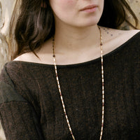 Woman wearing a vintage long 18k gold and garnet necklace against a neutral background penelopepenelope.com