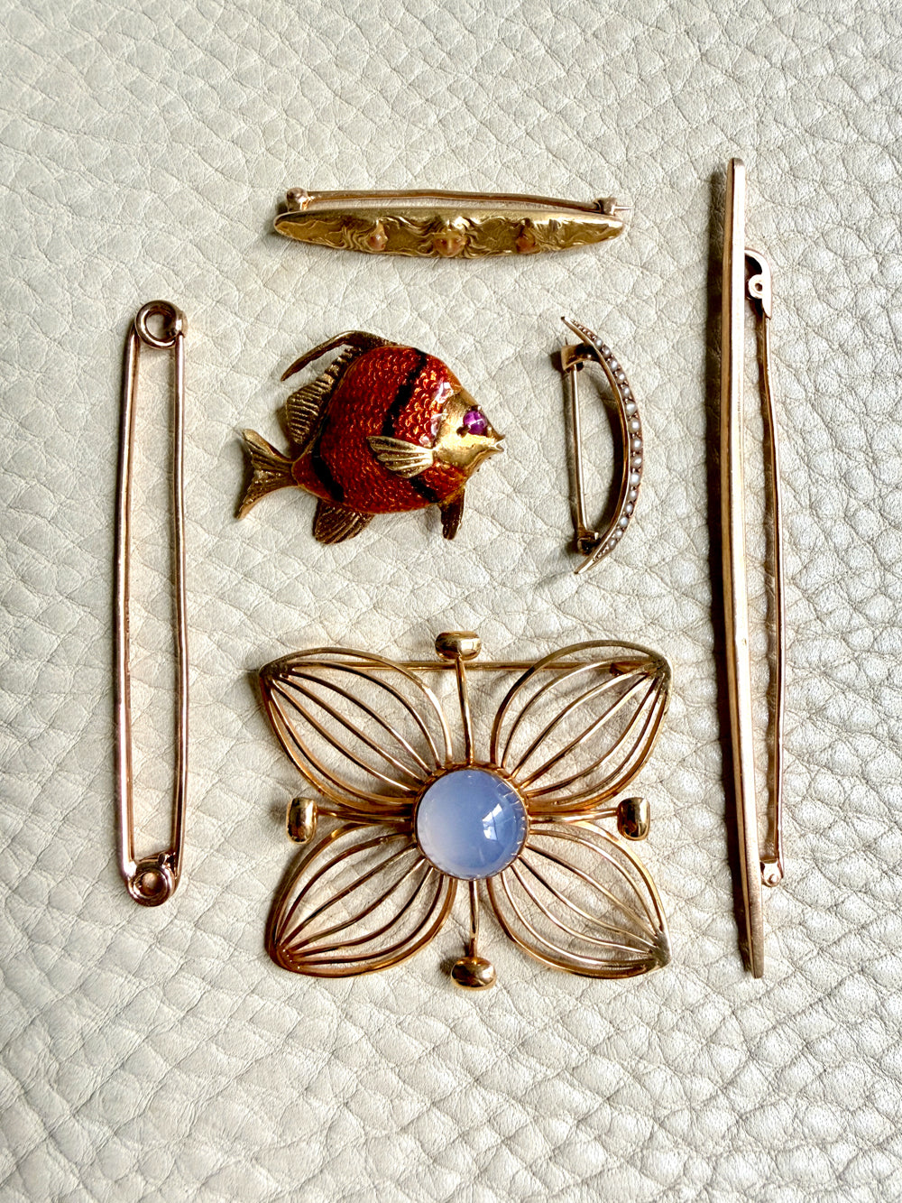 Collection of vintage brooches including a fish, flower, and other designs on a textured white background.