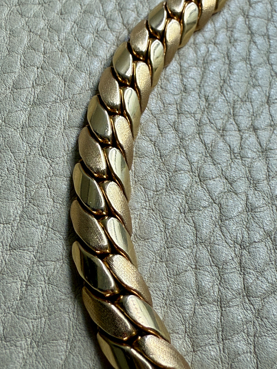 Gold chain bracelet on a textured light gray background