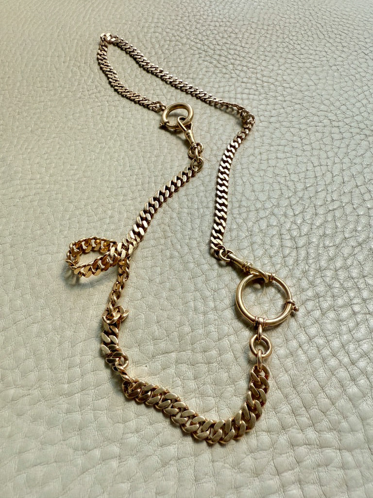 Gold chain necklace on a textured light gray background. PenelopePenelope.com